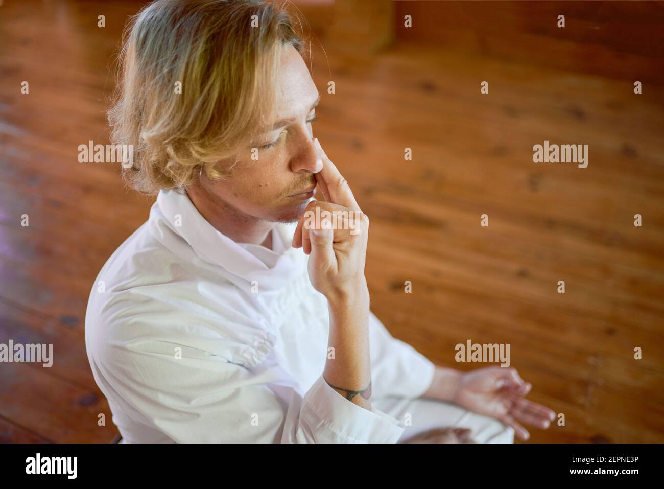 From above side view of crop young mindful male in white wear with closed eyes practicing nostril breathing on parquet Stock Photo