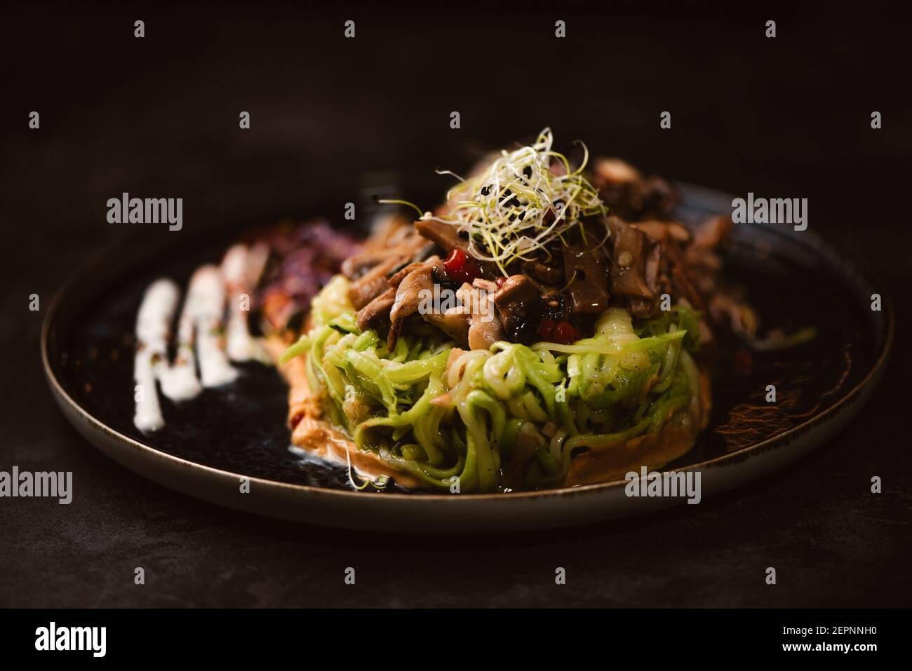 Yummy vegan dish with zucchini spaghetti and sauteed mushroom slices covered with red berries and alfalfa sprouts on dark background Stock Photo