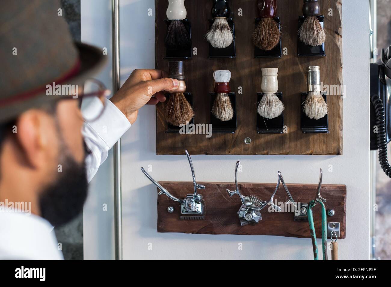 Crop stylish ethnic barber putting shaving tool on wall with different