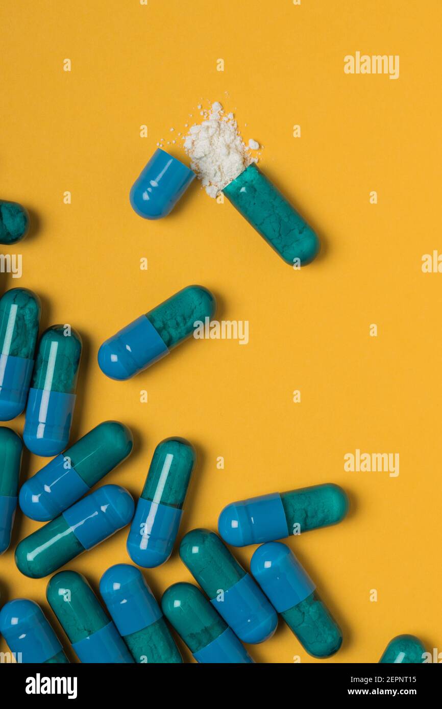 High angle of contents of medical drug poured out of blue colored capsule on yellow background