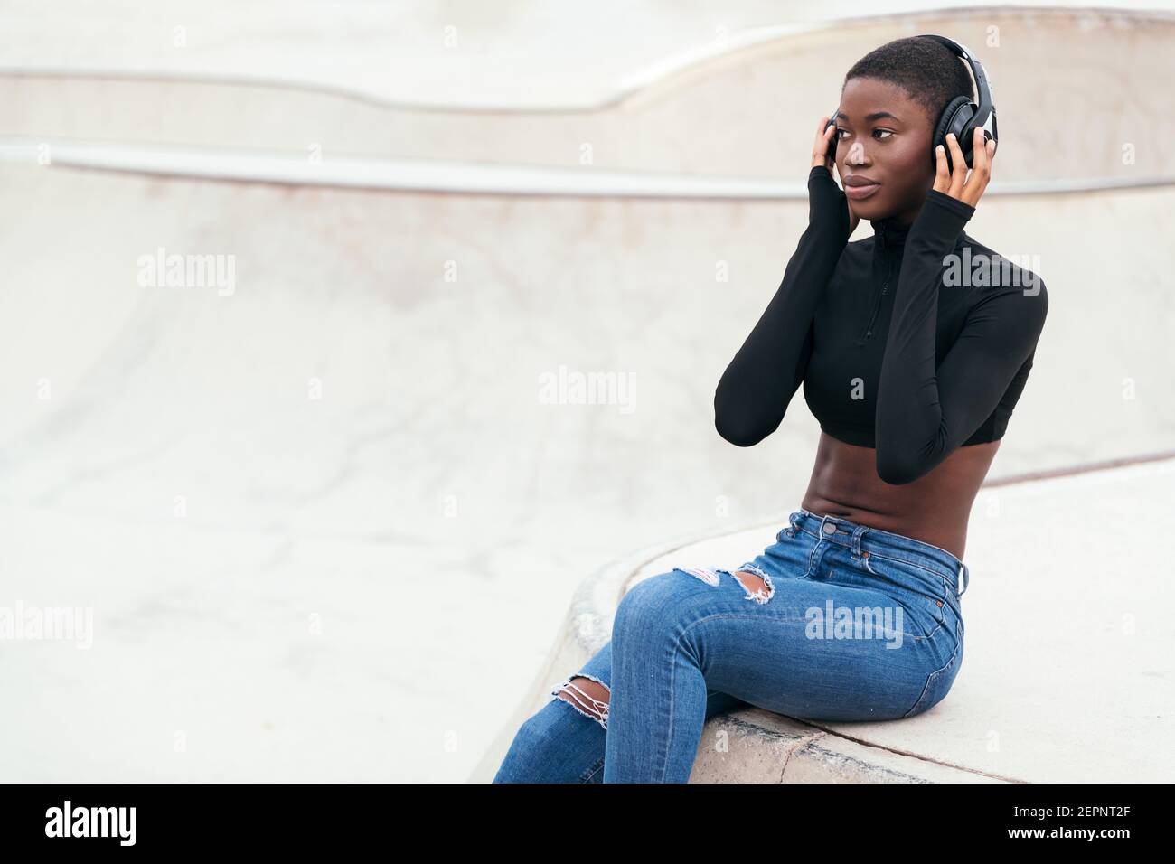 Side view of young contemplative African American female in ripped jeans  listening to music from wireless headphones while looking forward Stock  Photo - Alamy