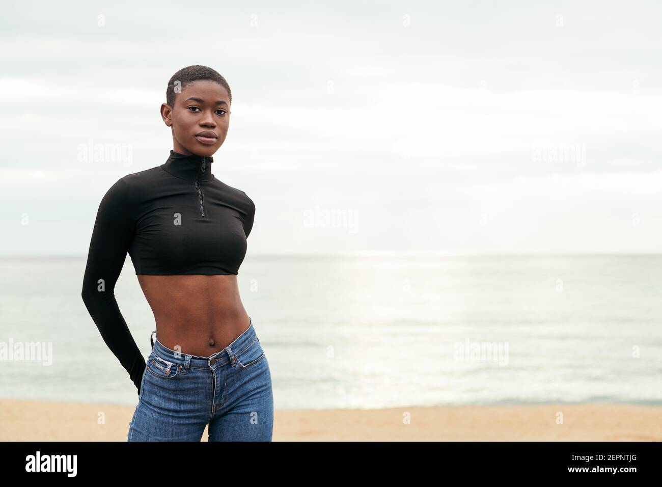 Young gentle African American female in casual clothes looking at camera on ocean coast Stock Photo