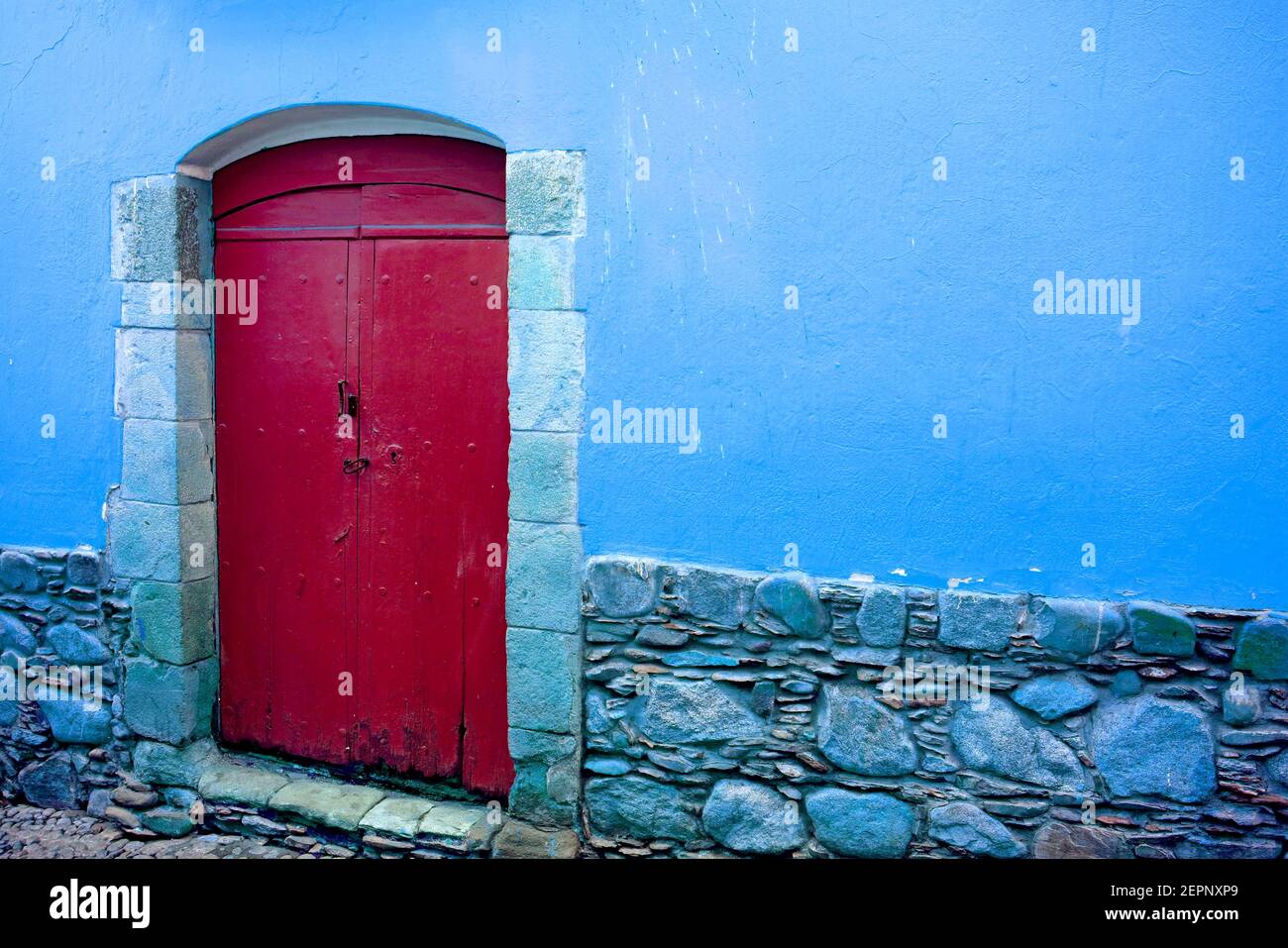 Red wooden door on blue wall of an old building Stock Photo