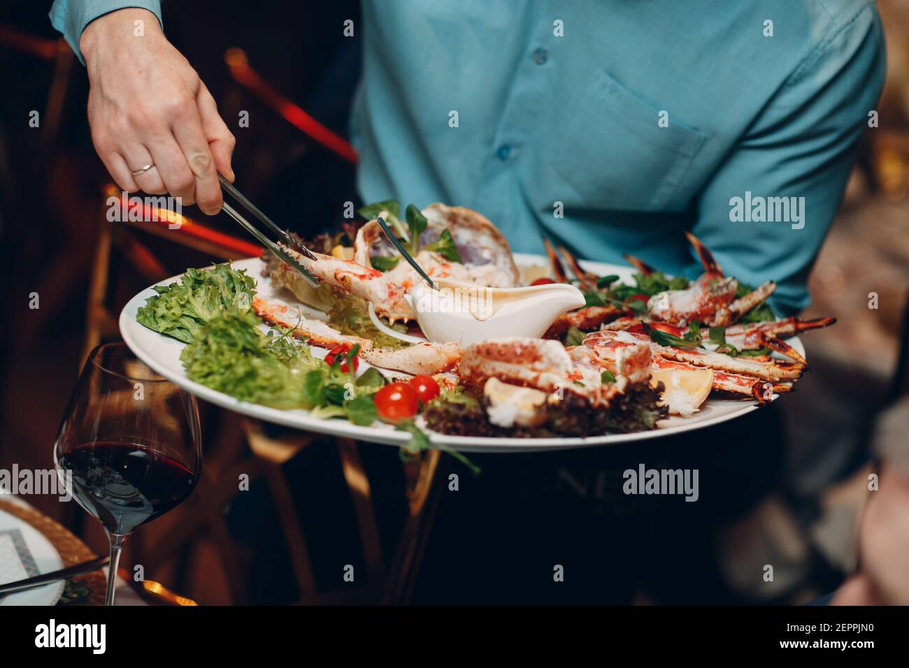 Waiter in a restaurant holds seafood dishes and serves a table catering Concept Healthy food octopus and crabs shellfish. Stock Photo