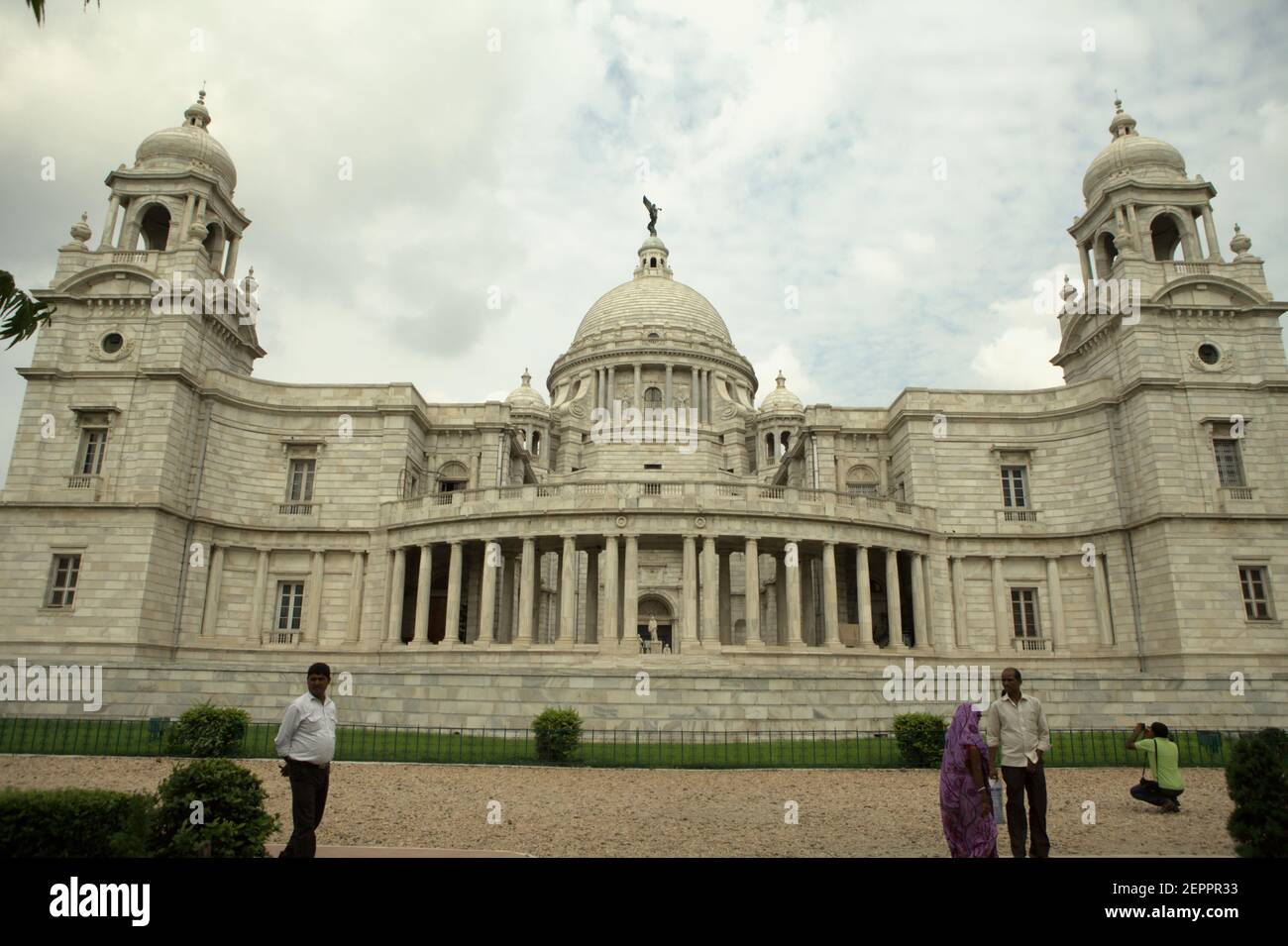 Visitors are photographed in a background of Victoria Memorial Hall in Kolkata, West Bengal, India. On the top of the hall's central dome is a figure of Angel of Victory, a goddess of ancient Greek mythology personifying victory. Stock Photo