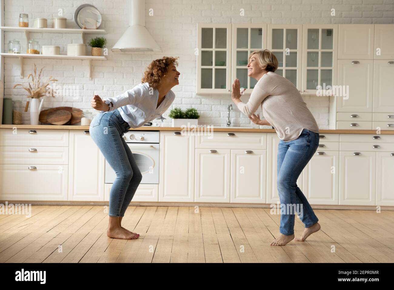 Adult daughter and mother dancing at modern kitchen celebrate renovation Stock Photo