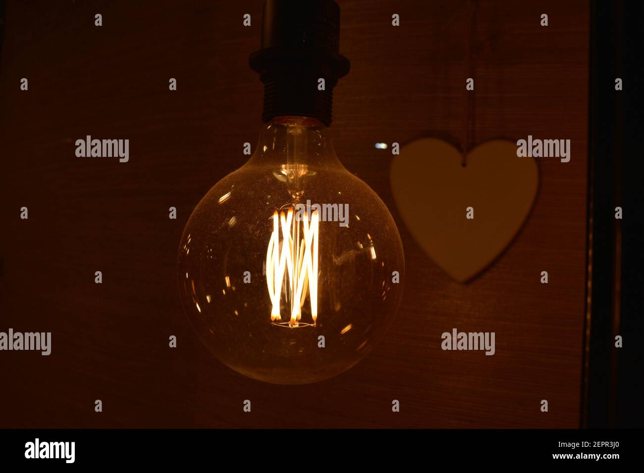 Glowing incandescent Edison light bulb closeup with heart in the background Stock Photo