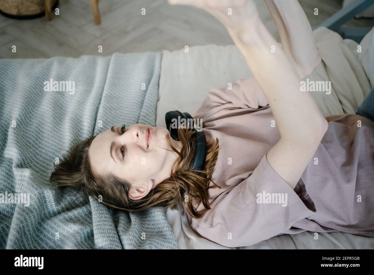 Creative woman is lying on bed with tablet, smiling thoughtful, writes a message, calls via video chat, reads the news. Work from home, freelance and Stock Photo