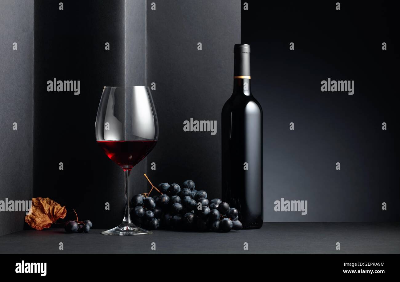 Red wine and blue grapes with driedup vine leave on a black background