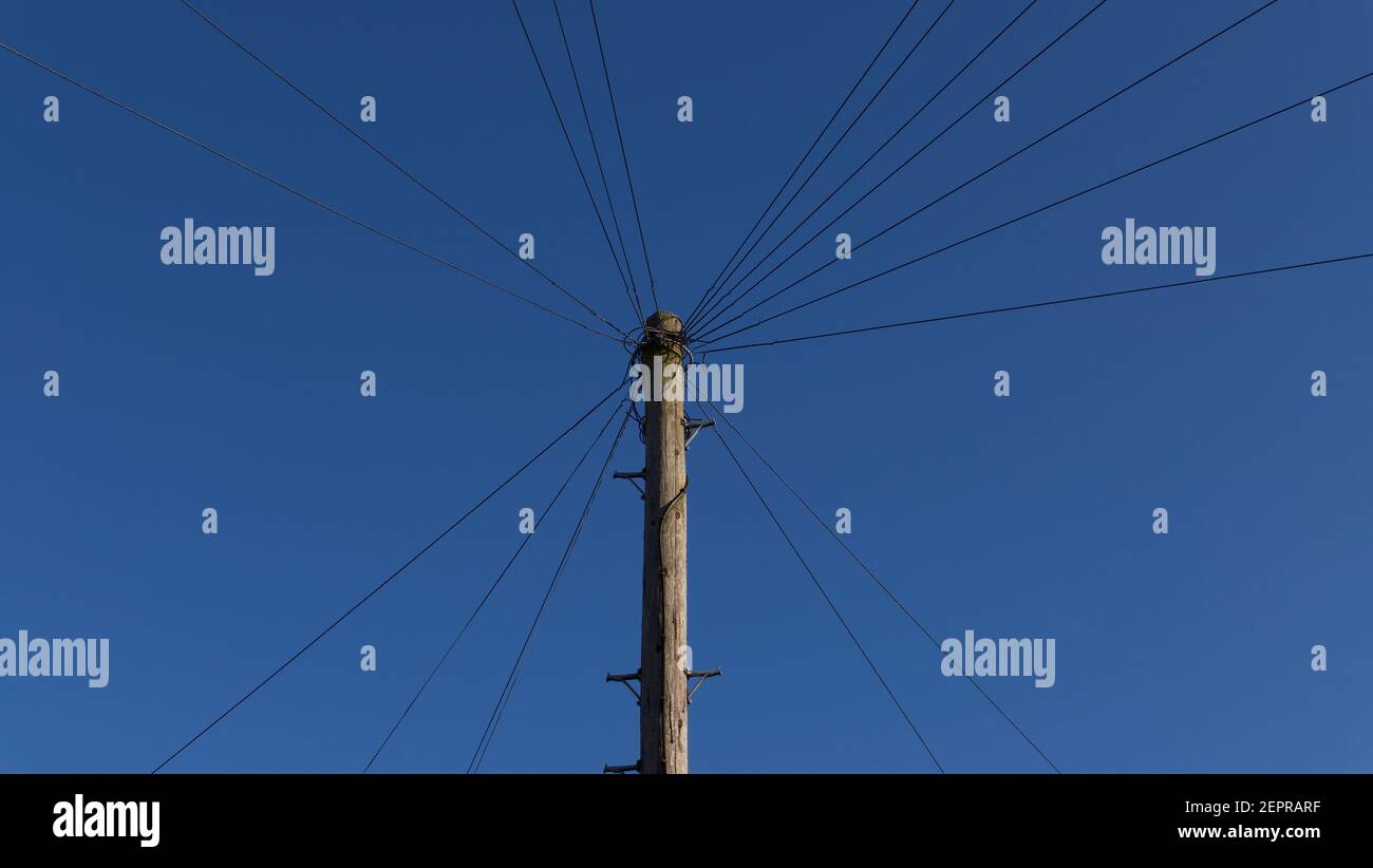 Wooden telegraph pole with wires leading off at angles against blue sky Stock Photo
