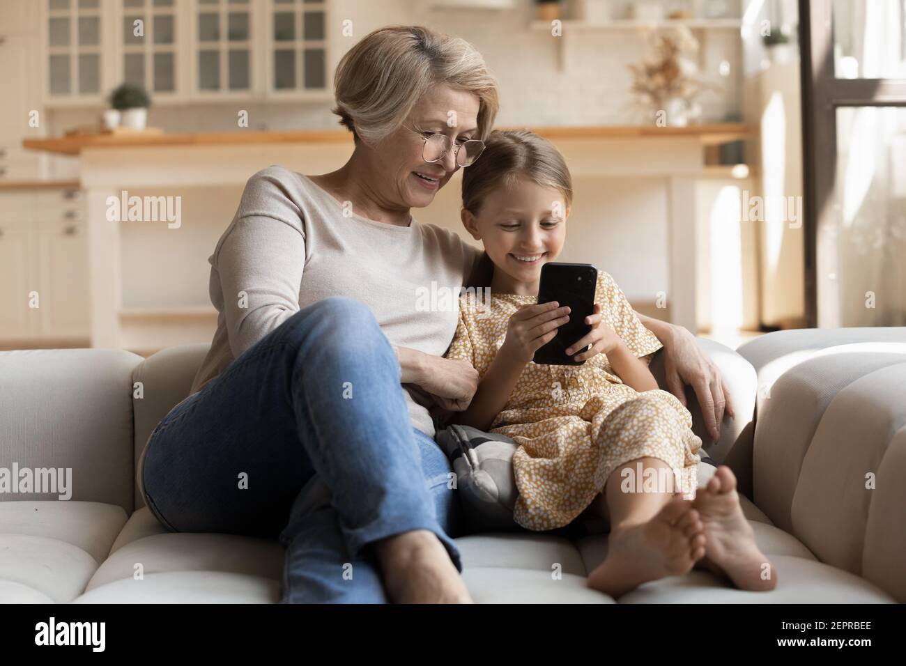 Happy girl and grandmother embrace on couch look at cell Stock Photo