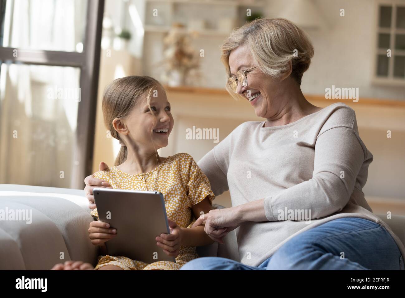 Laughing grandma hug small granddaughter discuss funny photo on pad Stock Photo