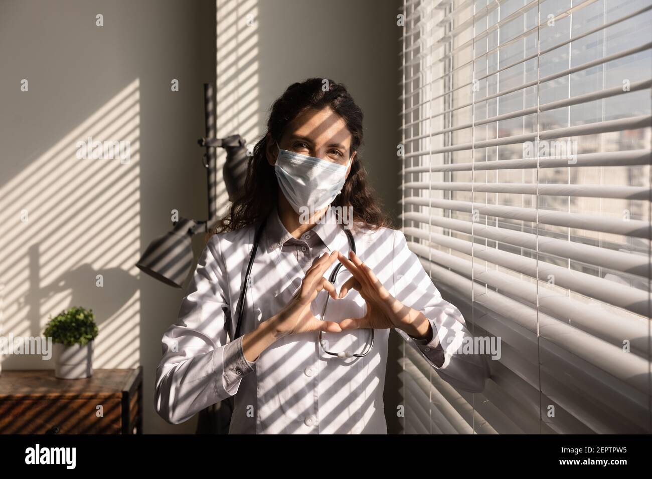 Portrait professional female doctor wearing medical mask showing heart gesture Stock Photo