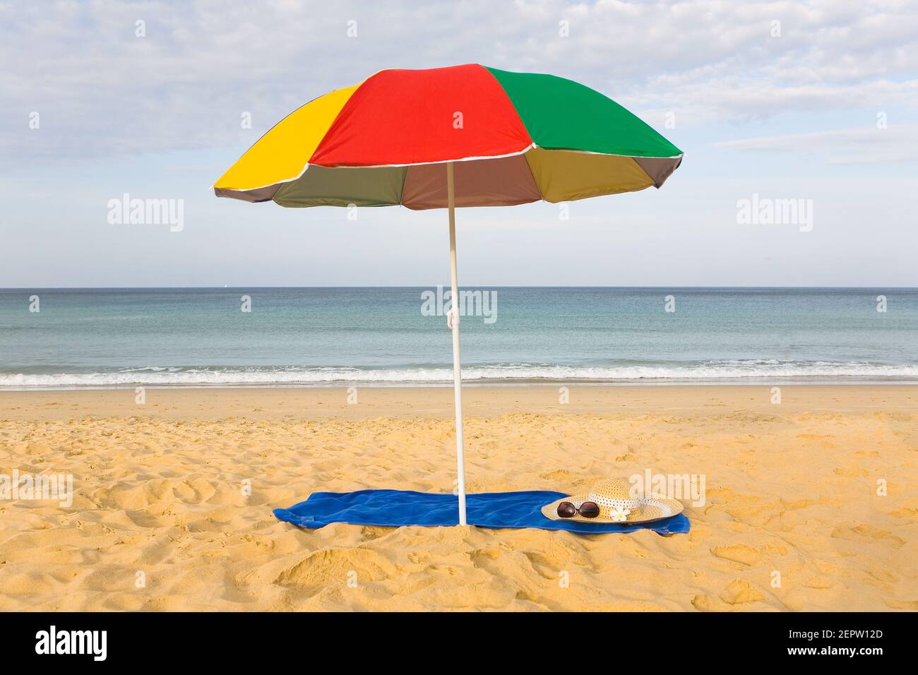 A beach umbrella over the bedspread on which glasses and a women's hat lie. Karon Beach in Phuket. Stock Photo