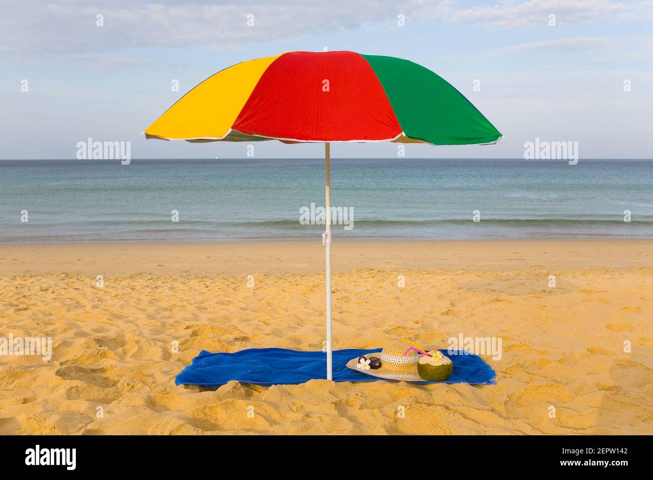 On the shore of a sandy beach under an umbrella lie sun glasses, a hat and a coconut fruit. Resort. Stock Photo
