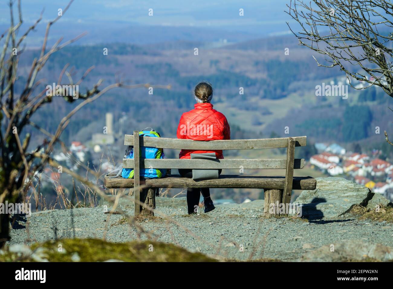 Schmitten, Germany. 28th Feb, 2021. A woman sits on a bench on the Feldberg plateau with a view of Reifenberg Castle. With temperatures around 2 degrees Celsius, many people make a trip to the local mountain in the Rhine-Main region. Credit: Andreas Arnold/dpa/Alamy Live News Stock Photo