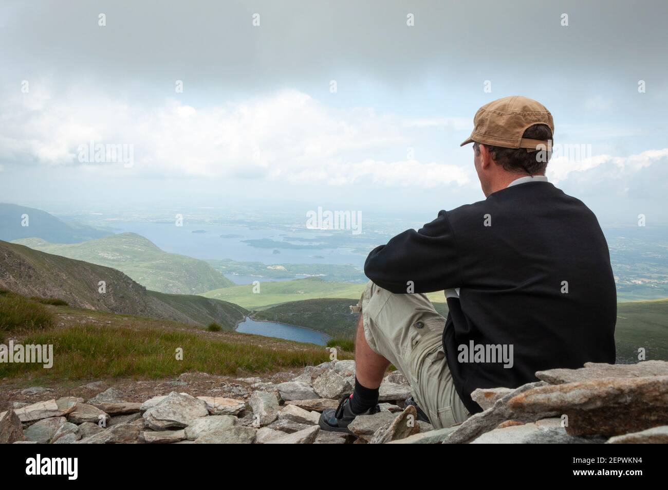 Lone male hiker at Mangerton Summit looking down to the Devil's Punch Bowl lake and the Killarney valley impressive landscape County Kerry, Ireland Stock Photo
