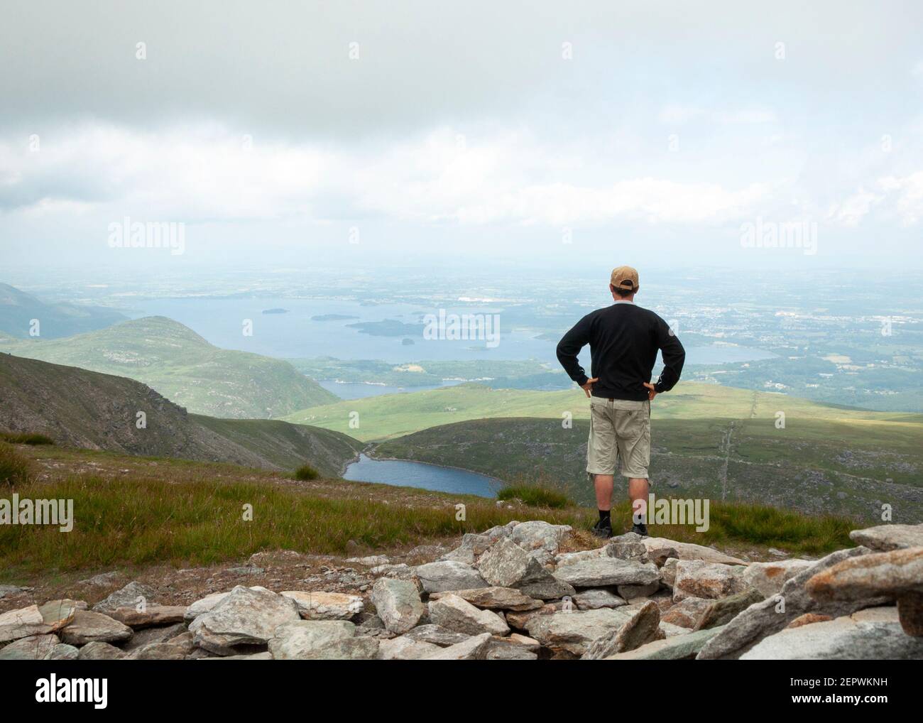 Lone male hiker at Mangerton Summit looking down to the Devil's Punch Bowl lake and the Lakes of Killarney impressive landscape County Kerry, Ireland Stock Photo
