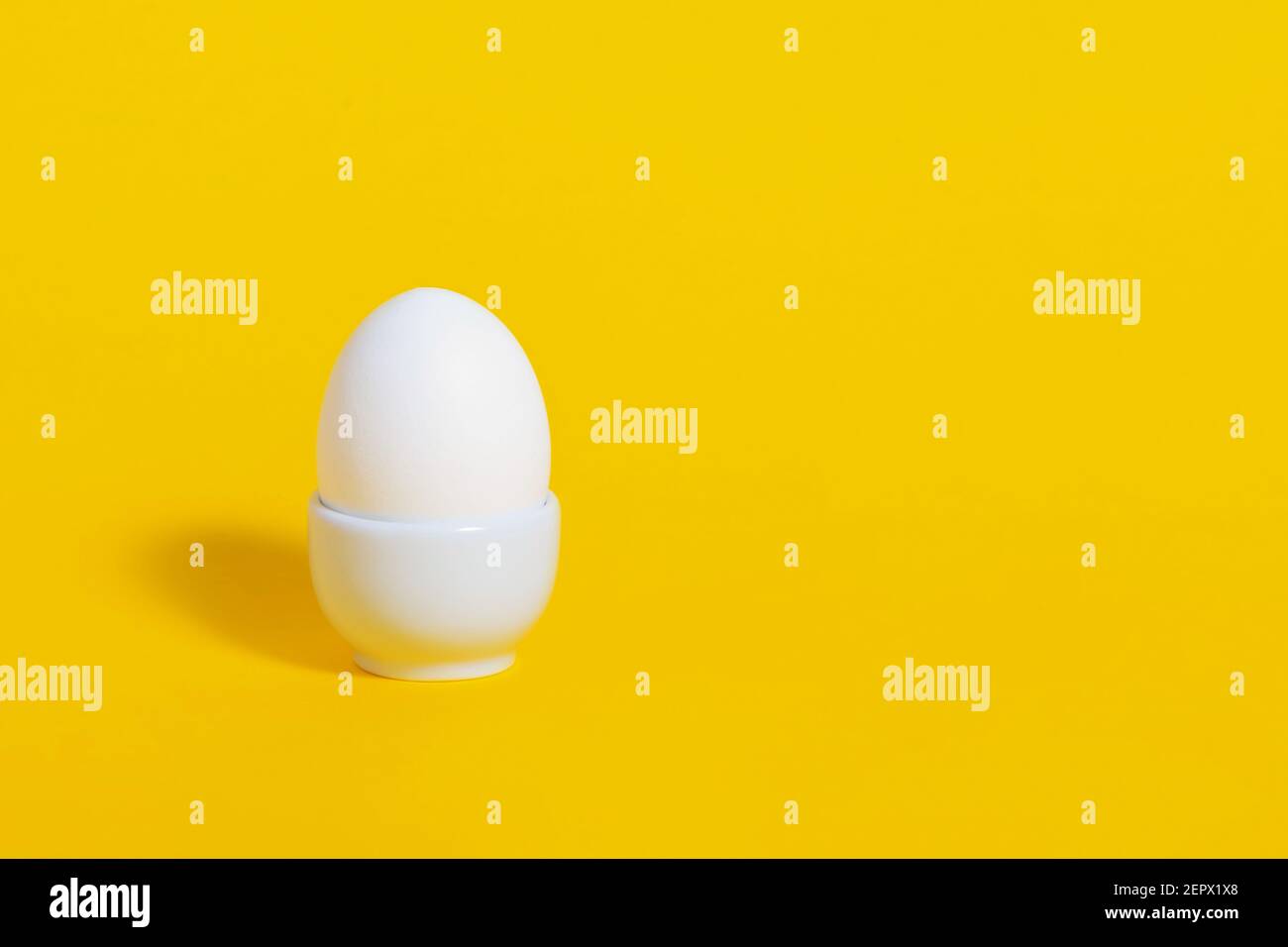 White chicken egg in white ceramic tray on bright, saturated yellow background. Easter breakfast concept. Copy space. Organic product, meal, food. Stock Photo