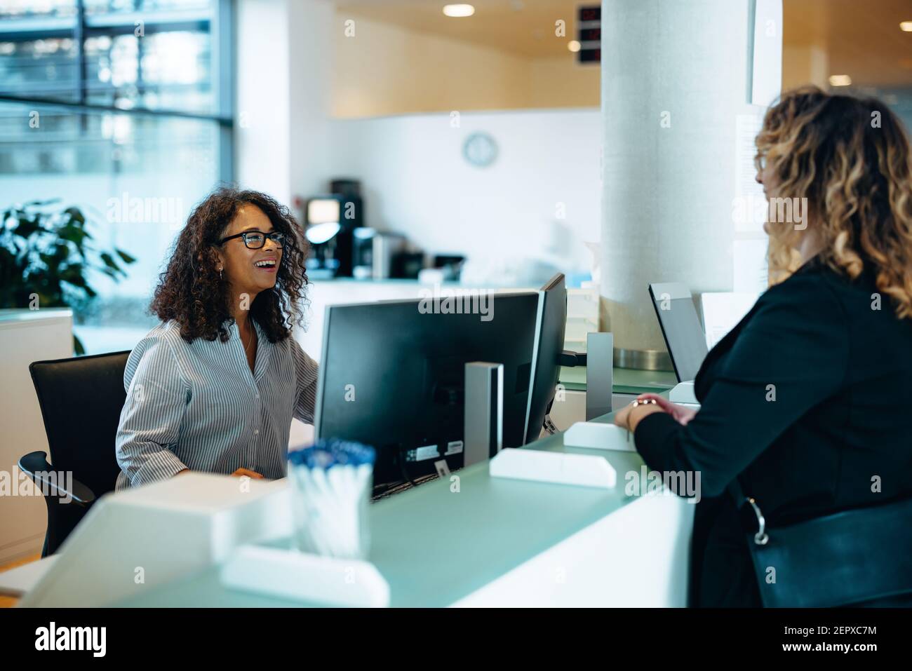 Receptionist assisting a woman standing at front desk. Woman standing