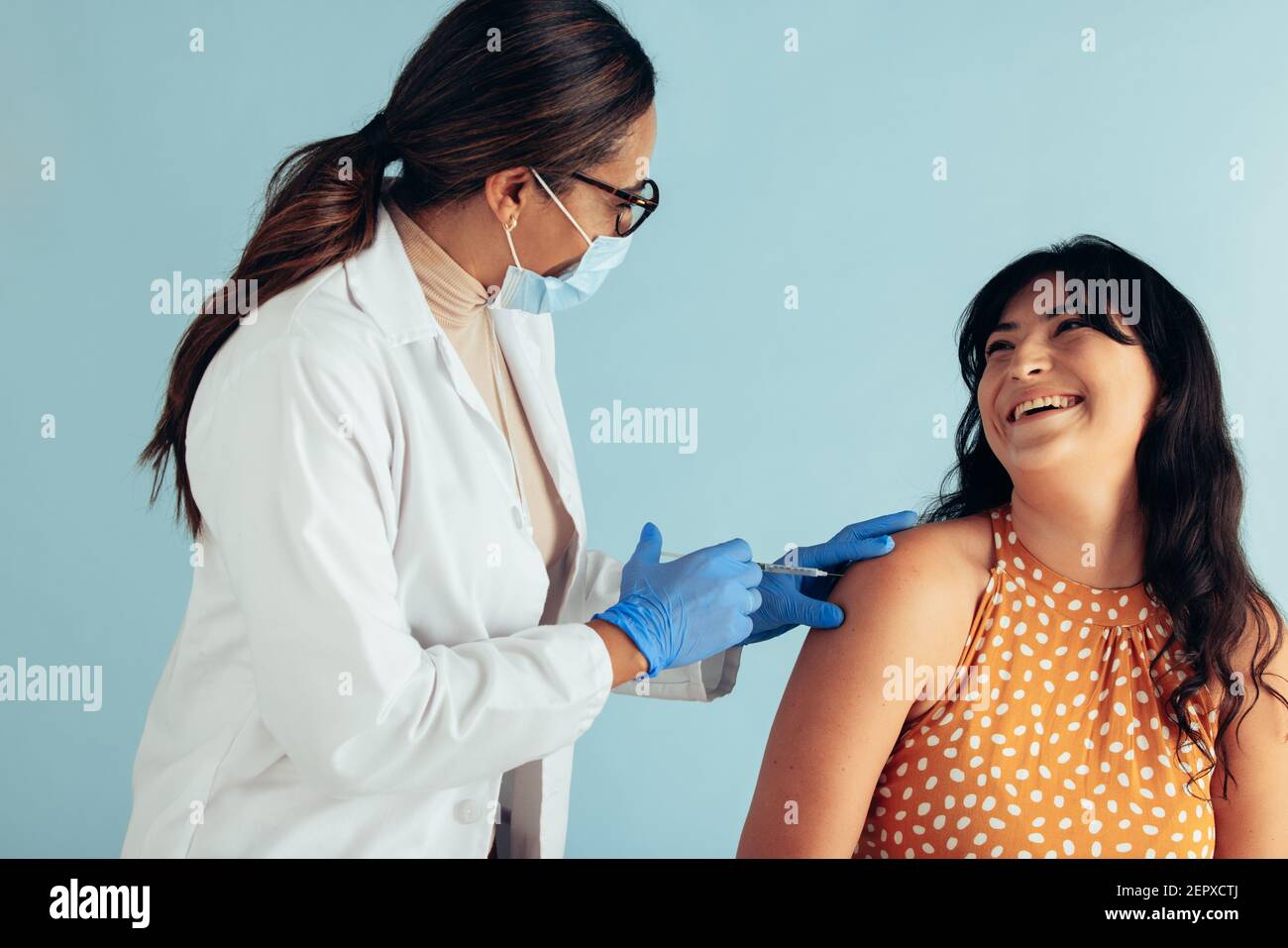 Smiling woman getting vaccinated. Doctor wearing face mask and protective gloves giving vaccine injection a happy female patient. Stock Photo