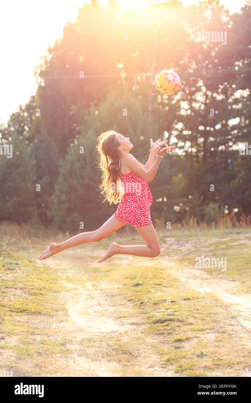 Portrait of Beautiful teenager girl  Is jumping and playing with ball at  summer sunset. Soft focused Stock Photo