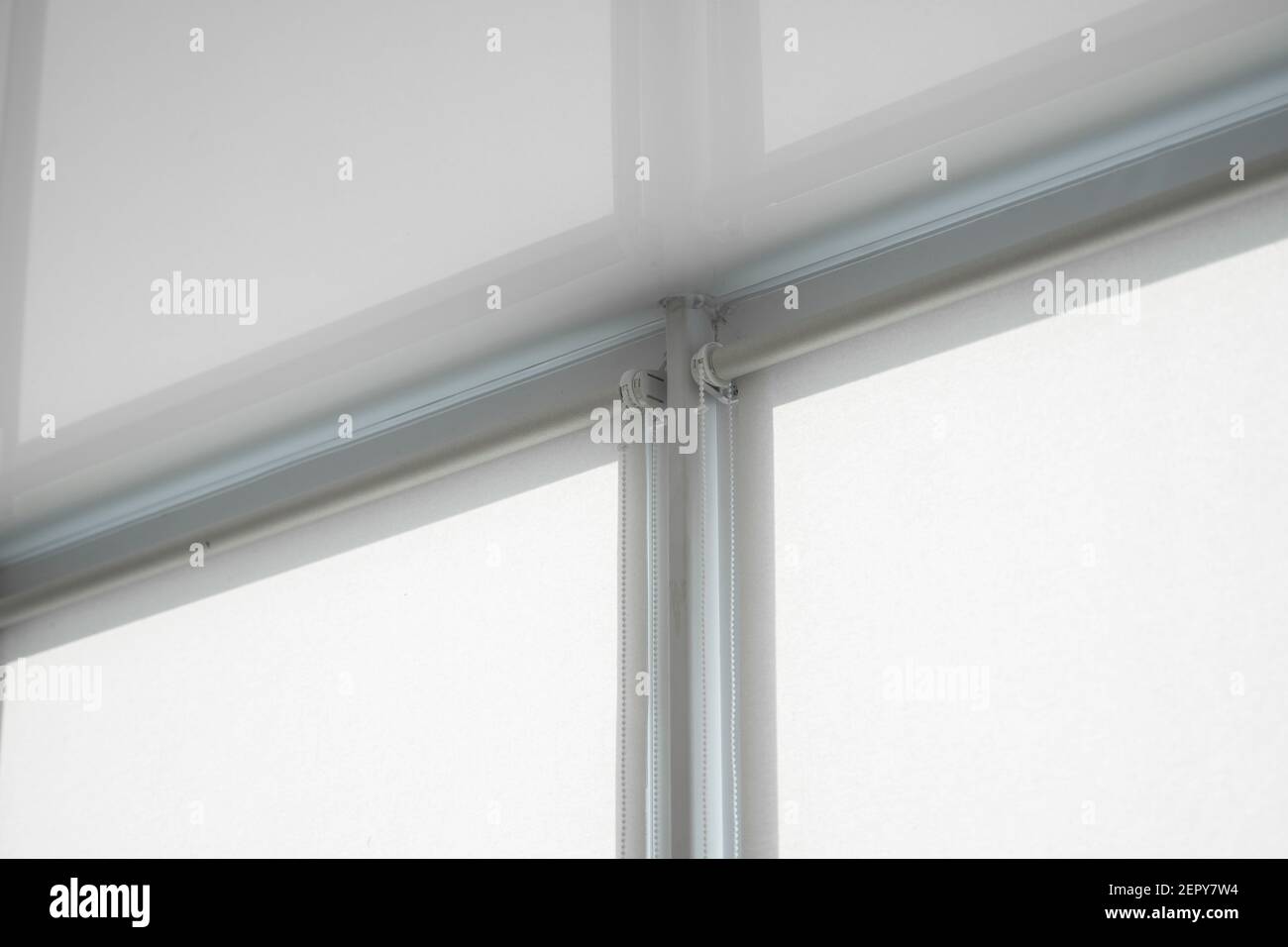 White fabric roller blinds on the plastic window on a balcony in the living room with a reflection in a stretch ceiling. Stock Photo