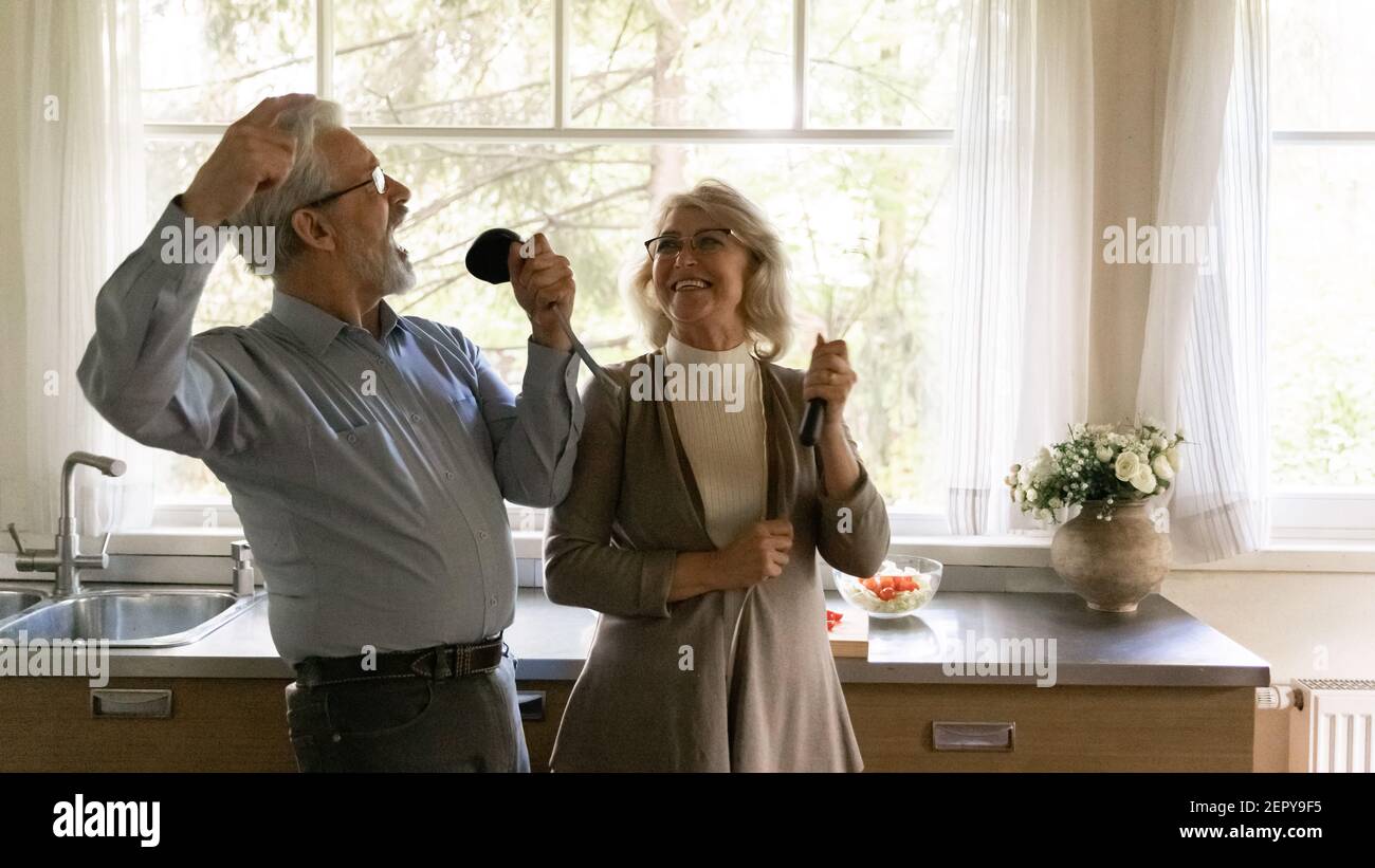 Excited happy mature family couple singing at utensils Stock Photo