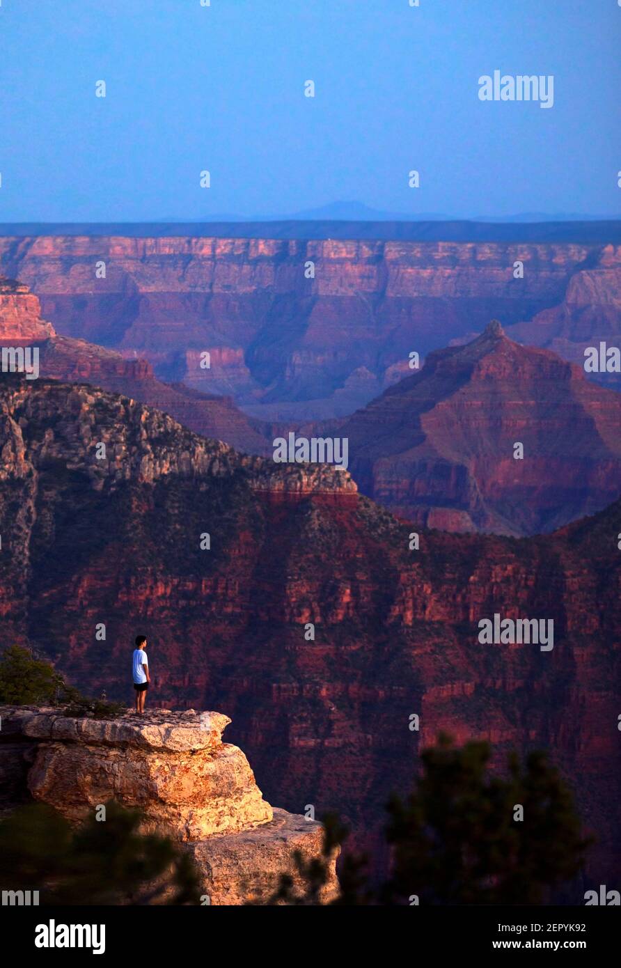 A young man stands on the edge of the Grand Canyon at sunset. Stock Photo