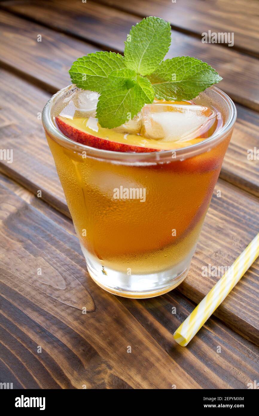 Cold tea with peaches in the glass on the brown wooden background ...