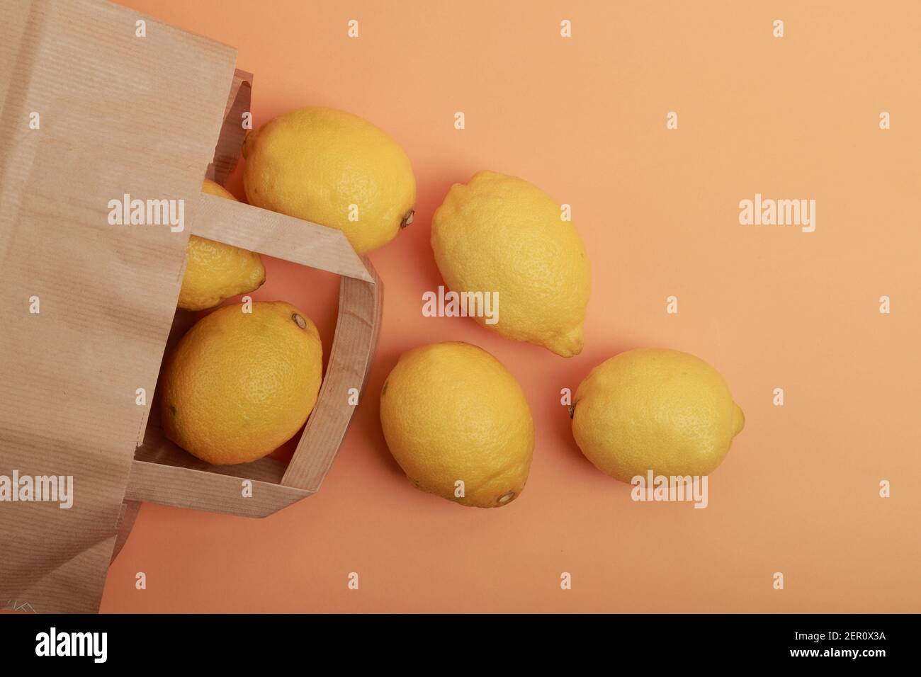 flat lay of several lemons coming out of a supermarket paper bag on orange background Stock Photo