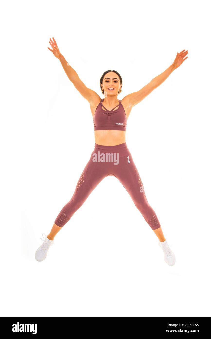 Vertical portrait of a young woman doing a star jump, isolated on a white background. Stock Photo
