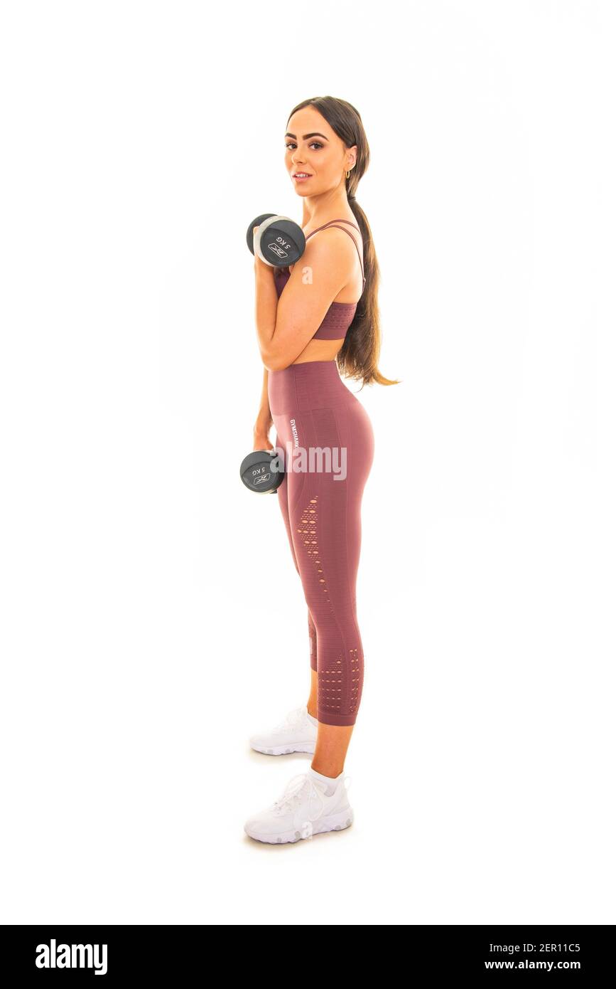 Vertical portrait of a young woman using dumbbells in a workout, isolated on a white background. Stock Photo