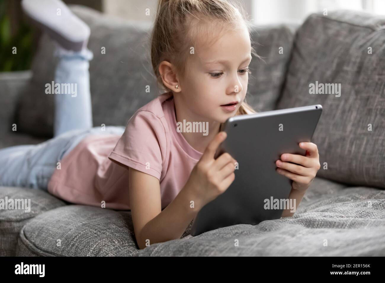 Focused cute preschooler girl watching movie, animated films Stock Photo