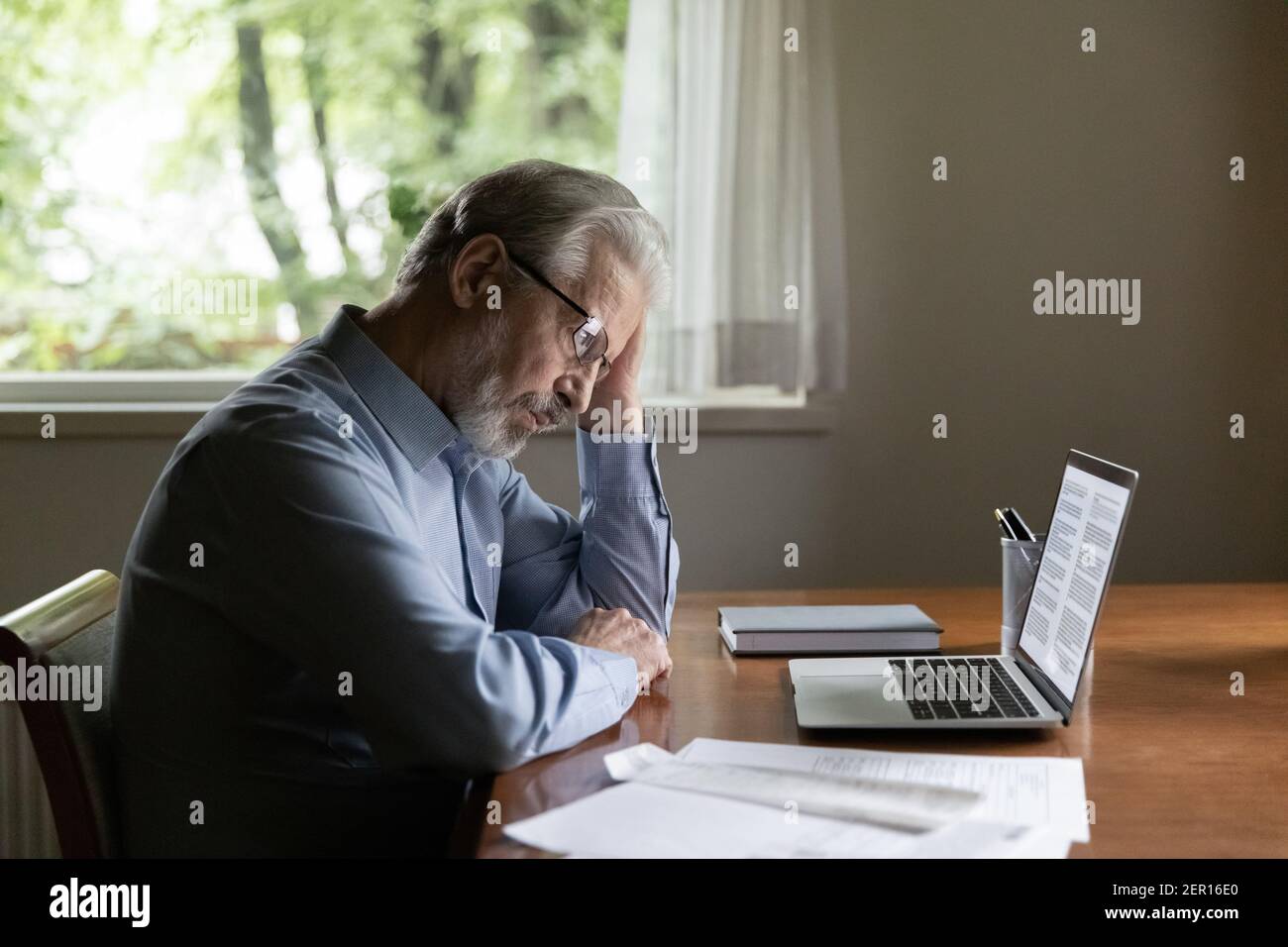 Focused pensive senior man working from home, using laptop Stock Photo