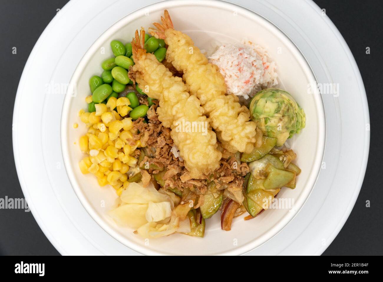 Overhead view of small bowl of poke topped with shrimp tempura, crab meat, edemame, and corn served up and ready to eat. Stock Photo
