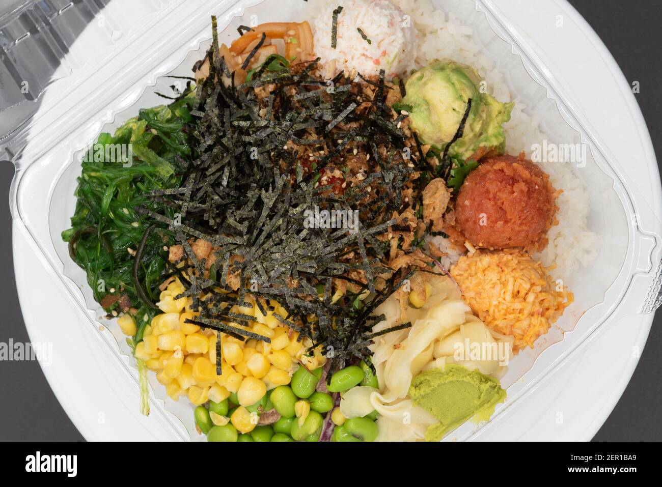 Overhead view of large takeout plastic bowl with three round scoops of poke topped with shrimp tempura, crab meat, edemame, and corn served up and rea Stock Photo