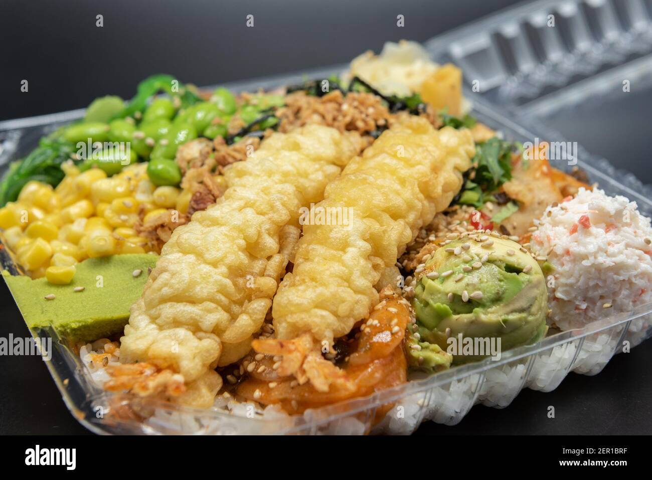 Takeout plastic bowl of poke topped with shrimp tempura, crab meat
