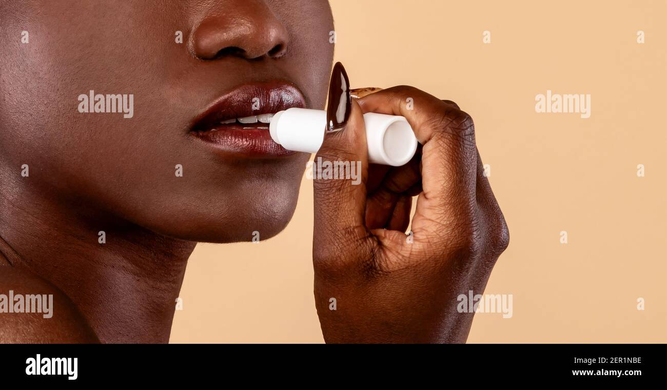 Black woman applying hygienic lip balm on light background Stock Photo