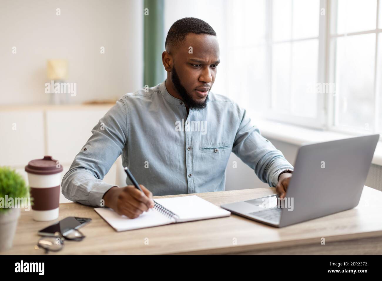 Black Businessman Working Taking Notes And Using Laptop At Workplace Stock Photo