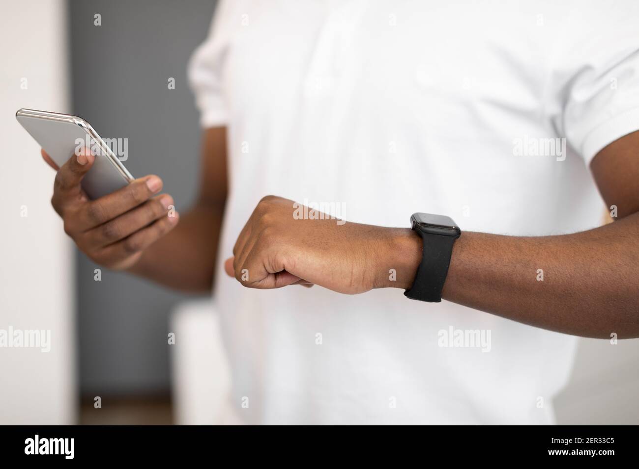 Unrecognizable Black Man Using Workout Gadgets Smartphone And Smartwatch Indoors Stock Photo