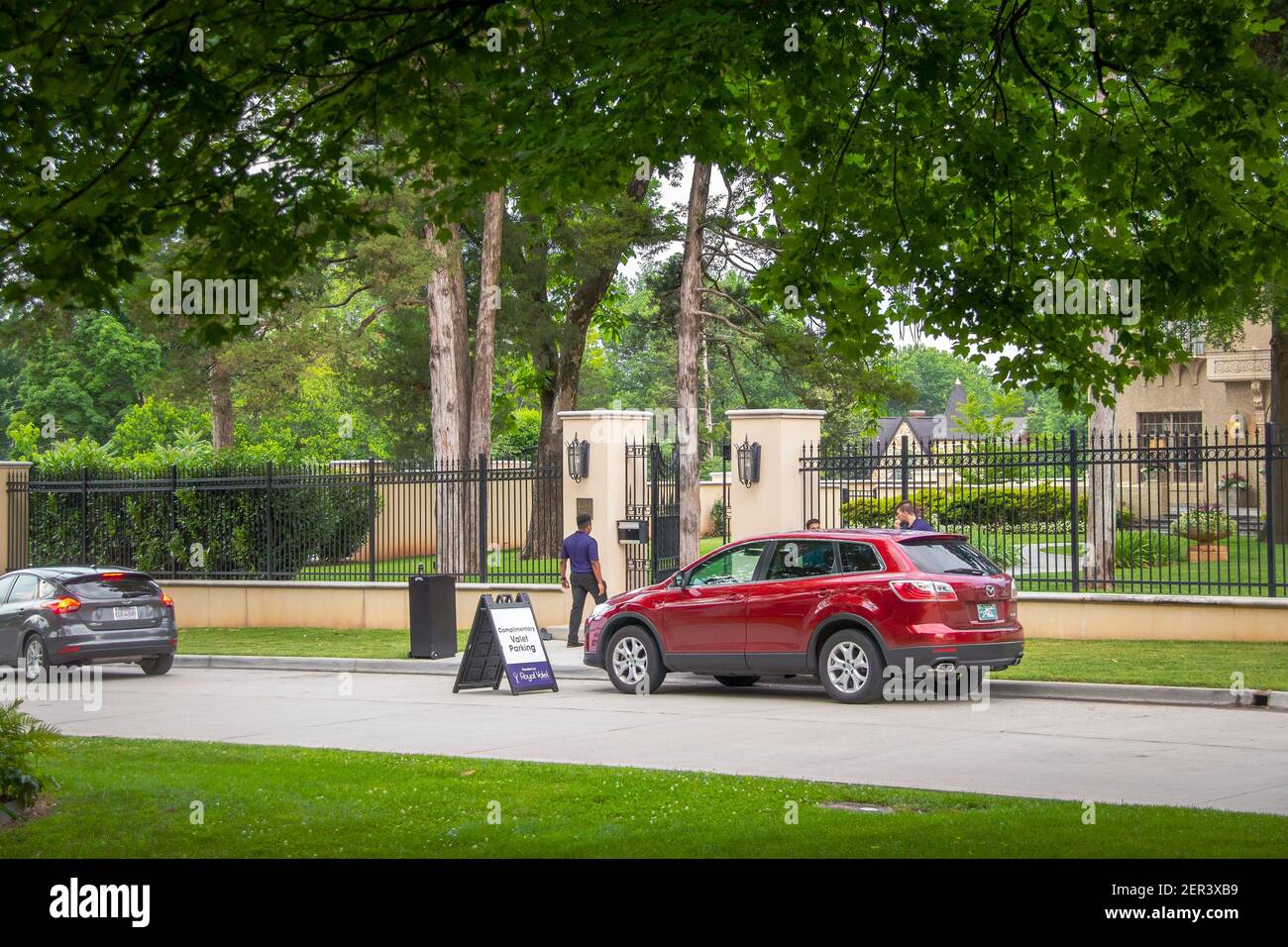 06-01-2019 Tulsa USA  Valet parking on neighborhood street outside luxious fenced estate with many tall trees. Stock Photo