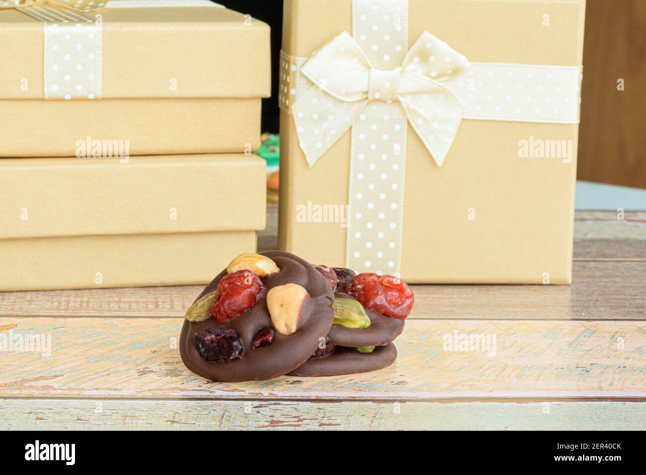 Three chocolate chip cookies with nuts. Small golden gift boxes in the background. Stock Photo