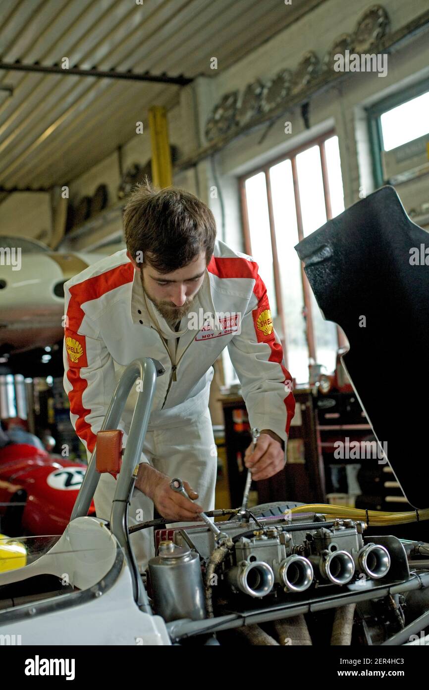 Good looking car mechanic working in garage on repair of racing car motor Stock Photo