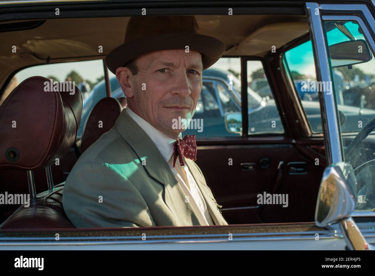 Man with suit and bow tie sitting inside his Mercedes 280SE, at Goodwood Revival, Chichester, West Sussex, England Stock Photo