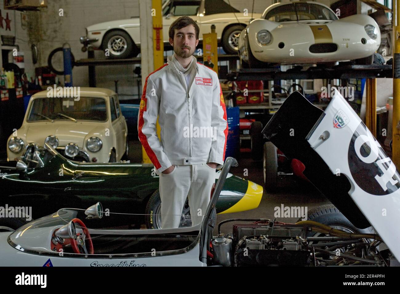 Portrait of young race car driver standing at classic garage workshop. Stock Photo