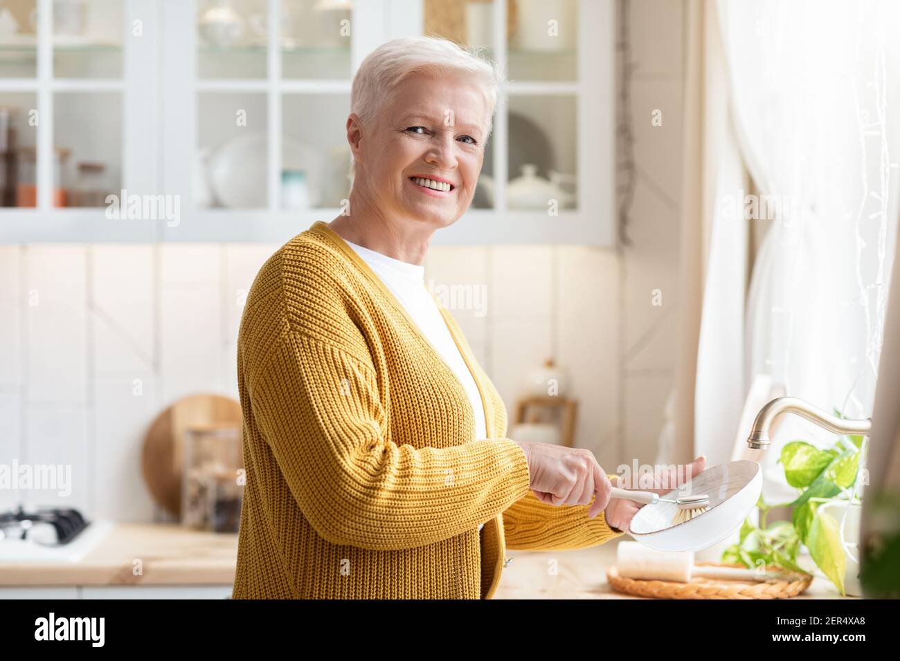 https://c8.alamy.com/comp/2ER4XA8/cheerful-senior-woman-washing-dishes-in-kitchen-2ER4XA8.jpg