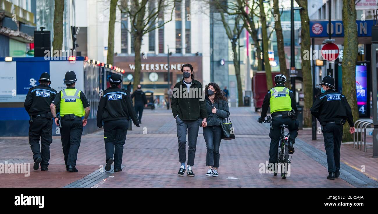 Birmingham, United Kingdom, UK. 28th February 2021: A masked couple walk hand in hand along New Street as an increased police presence can be seen through the city, as part of Project Servator (tackling knife crime and terrorism) and policing COVID restrictions. Credit: Ryan Underwood / Alamy Live News Stock Photo