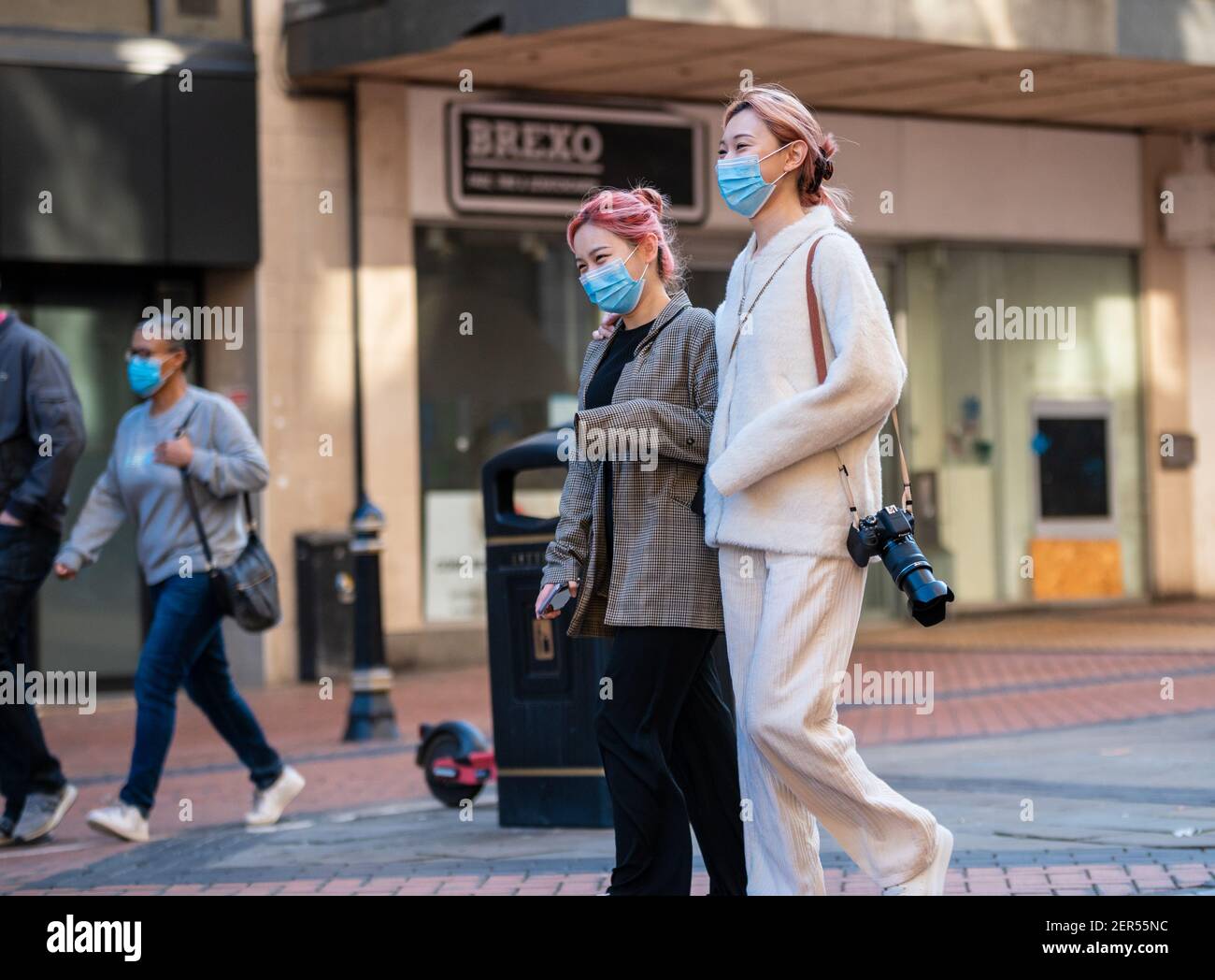 Birmingham, United Kingdom, UK. 28th February 2021: Two happy masked women with one hand over the others shoulder, enjoy the sun shine while walking down New Street in the city centre. Credit: Ryan Underwood / Alamy Live News Stock Photo