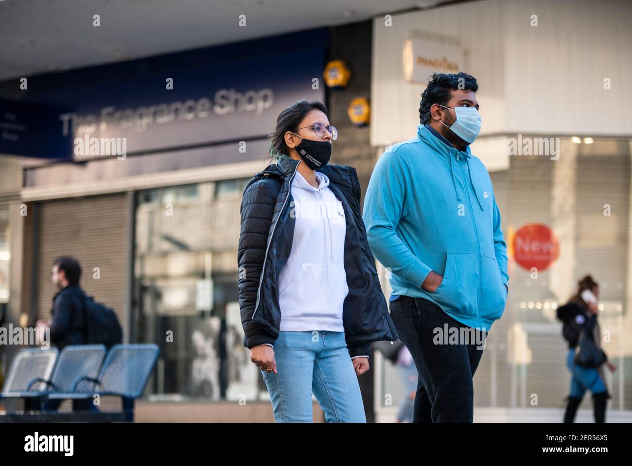 Birmingham, United Kingdom, UK. 28th February 2021: Two students, one wearing a University of Birmingham branded face-mask walk along Birmingham city centre's High Street during a sunny Sunday, the last day of February. Credit: Ryan Underwood / Alamy Live News Stock Photo